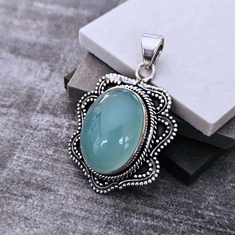 Chelcedony stone pendant with silver decorative frame on a textured surface