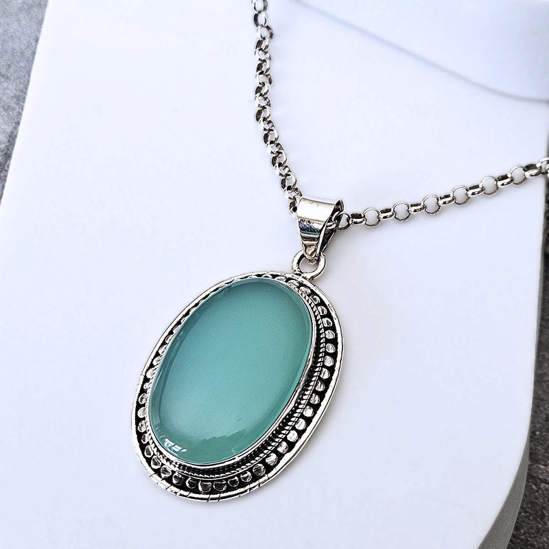 A silver-tone oval pendant necklace with a smooth, light green cabochon stone, displayed on a white surface.