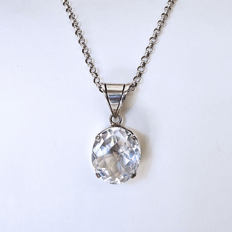 A silver-toned necklace with a faceted clear oval gemstone pendant, displayed against a plain white background.