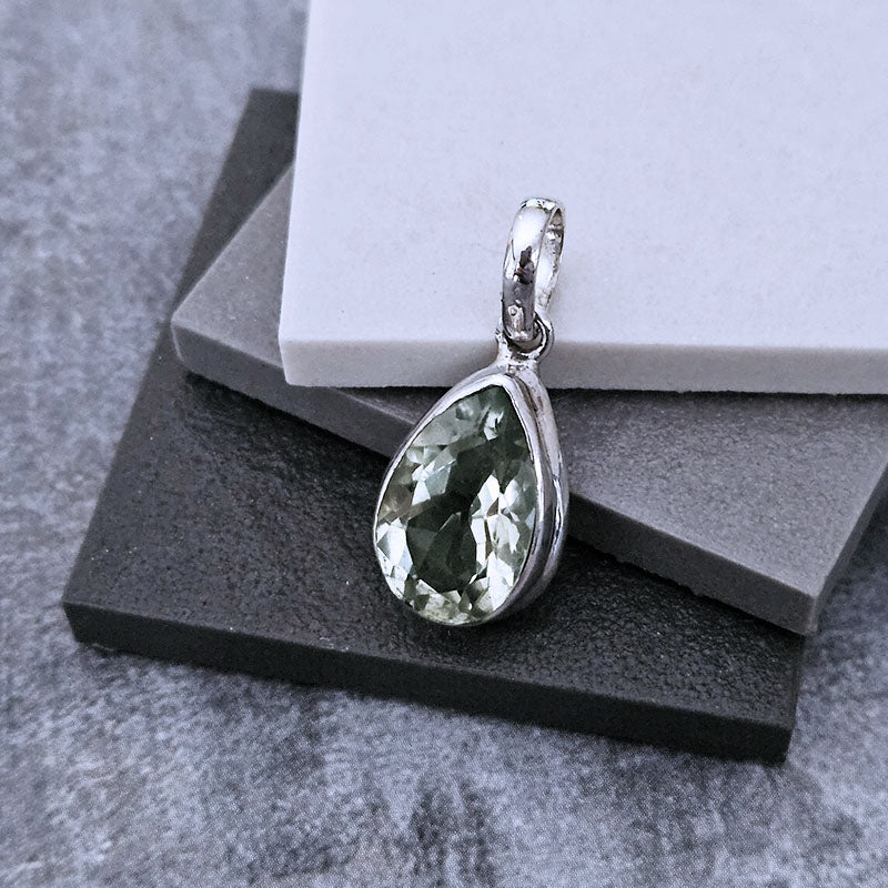 Silver pendant with a green gemstone on a gray surface