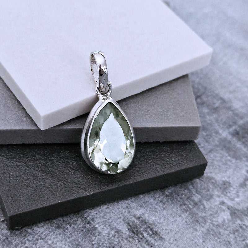 Teardrop-shaped silver pendant with a green gemstone on a gray surface