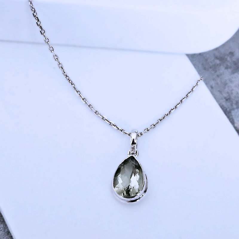 Teardrop-shaped pendant on a chain against a light blue background