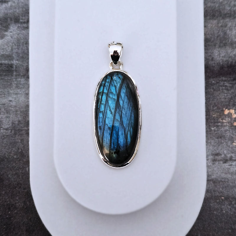 Blue labradorite pendant on a white stand with a gray background