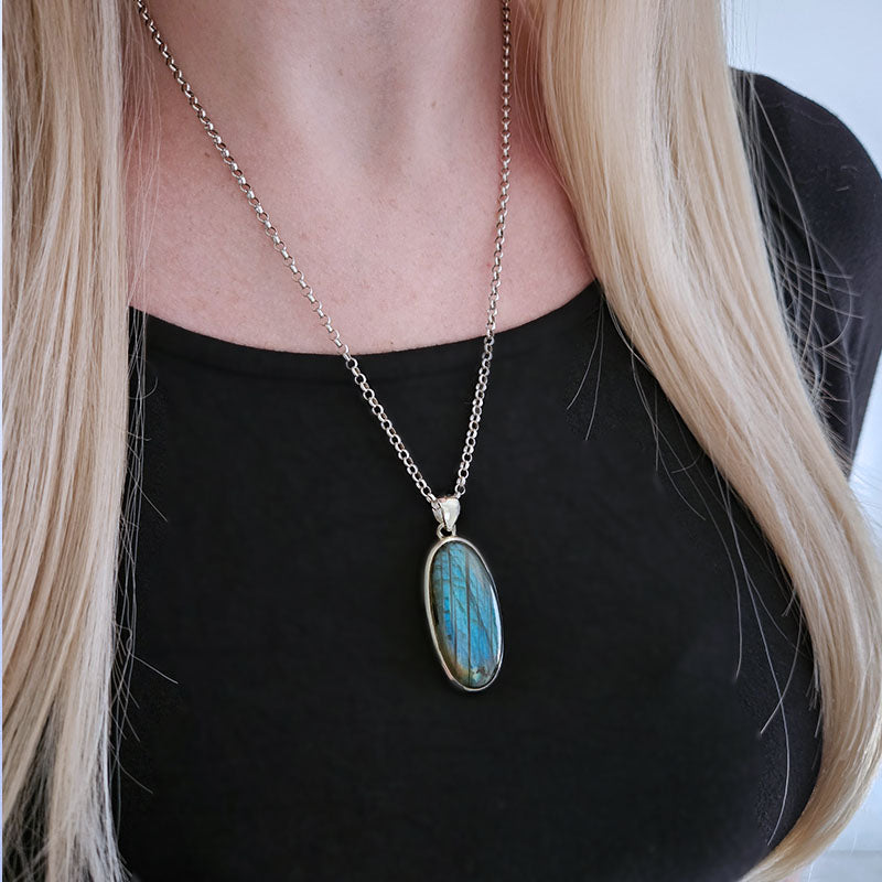 Necklace with a blue pendant worn by a person against a black background