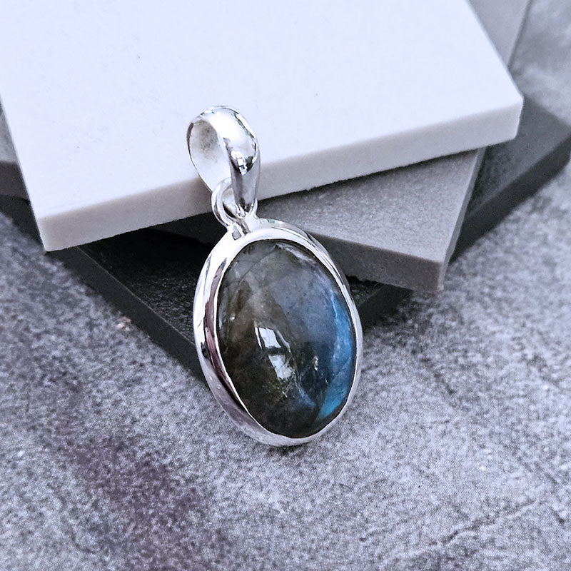 Silver pendant with a blue gemstone on a textured surface