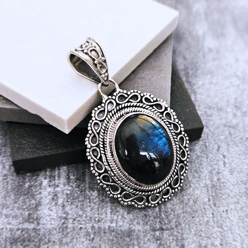 Silver pendant with a blue gemstone on a textured surface