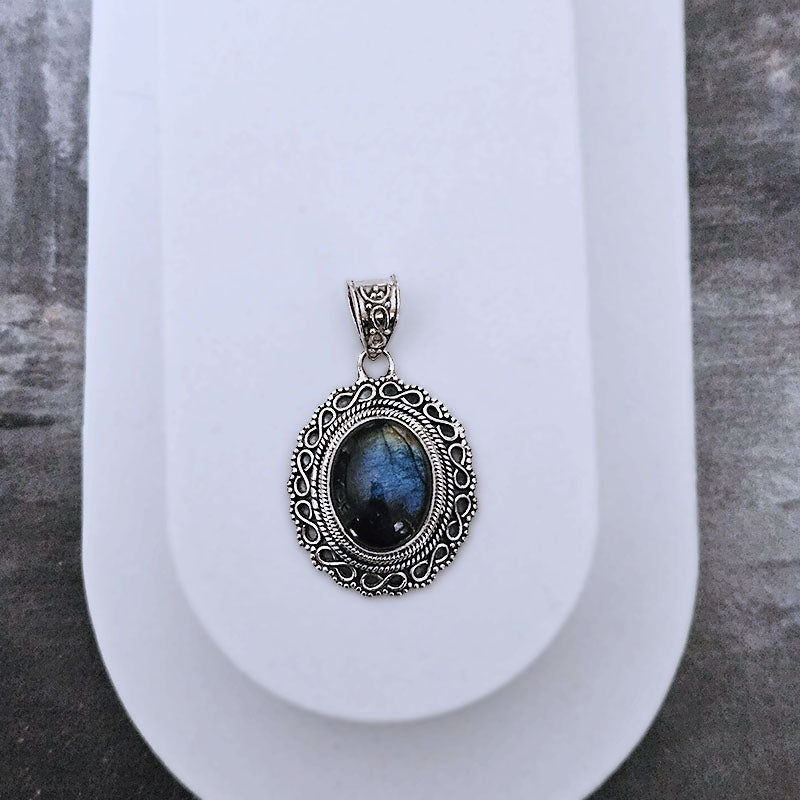 Silver pendant with a blue gemstone on a white stand against a gray background