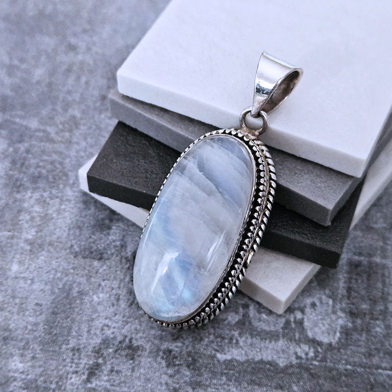 Silver pendant with a light blue stone on a textured surface