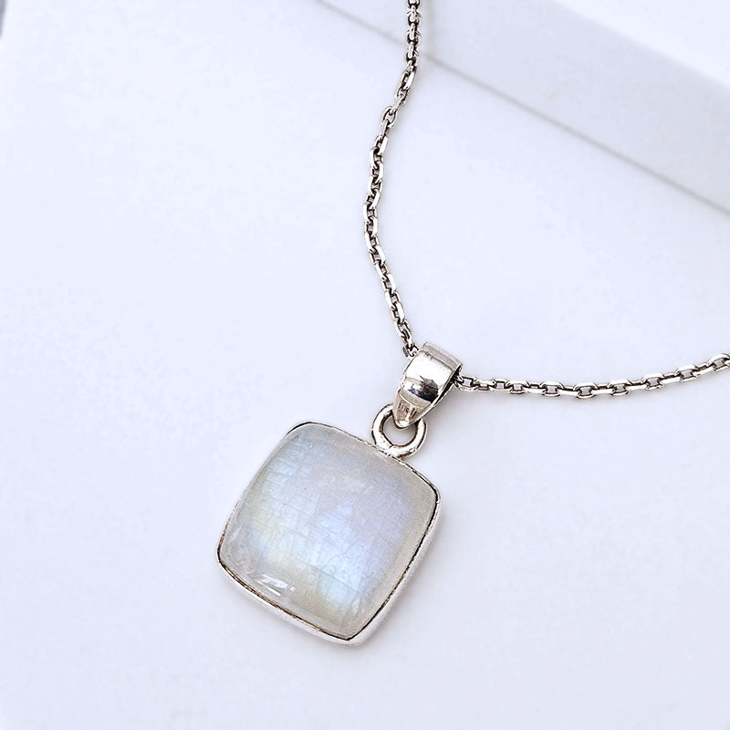 A silver chain necklace with a square pendant featuring a milky white iridescent stone, displayed on a clean white surface.