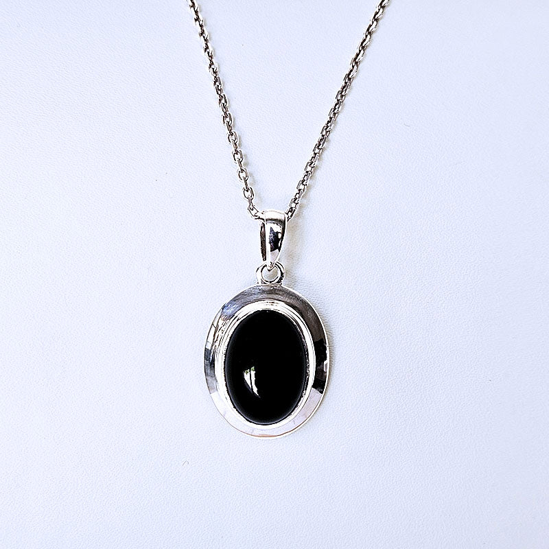 Silver necklace with a black pendant on a light gray background