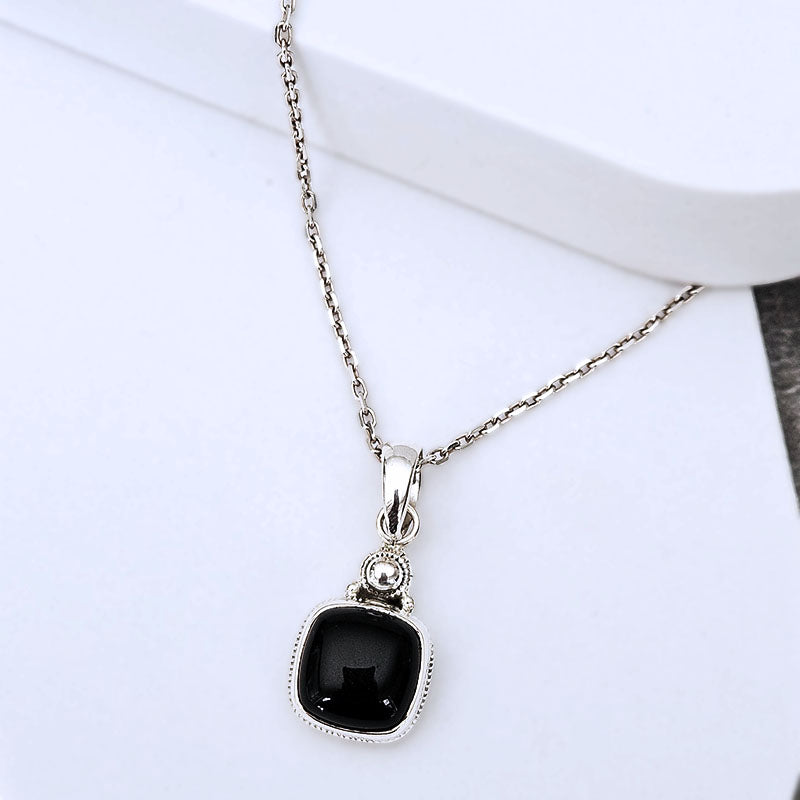 A silver-toned necklace with a square black pendant, displayed on a clean white surface.