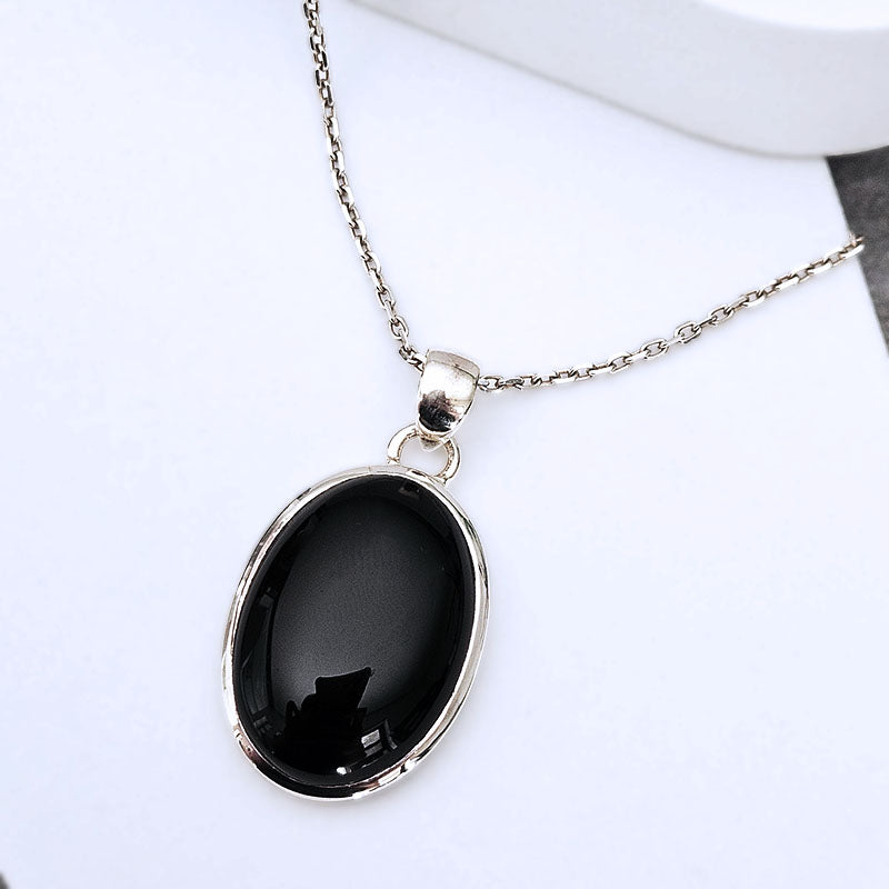 A silver chain necklace with an oval black onyx pendant in a polished silver bezel setting, displayed on a clean white surface.