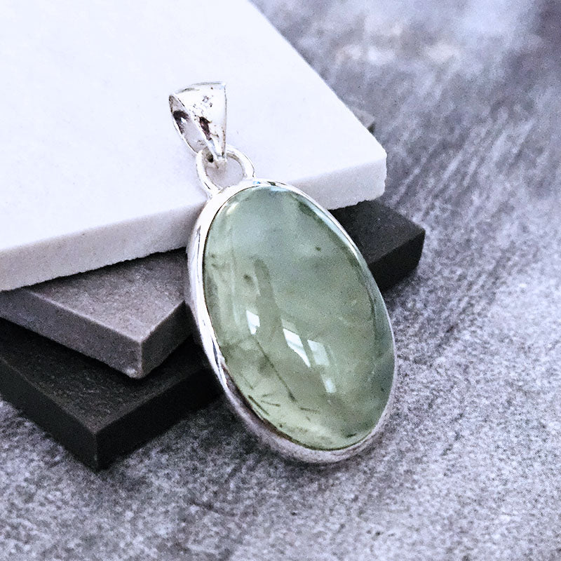 Green Prehnite gemstone pendant in silver setting on a gray surface