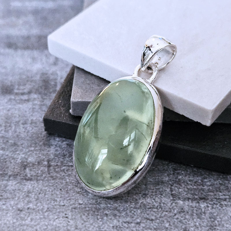 Green Prehnite gemstone pendant on a silver chain against a neutral background