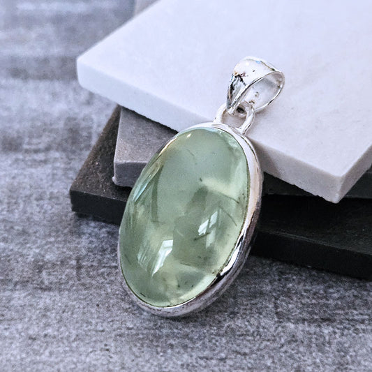Green Prehnite gemstone pendant on a silver chain against a neutral background