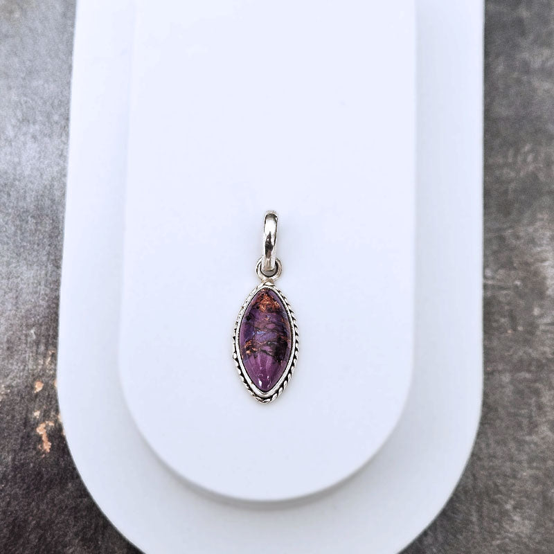A silver bezel-set marquise-shaped pendant featuring a turquoise gemstone with natural inclusions, displayed on a white jewelry stand.
