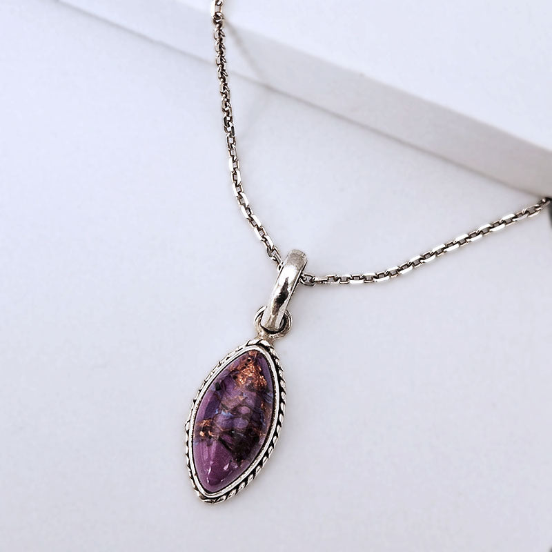 A silver-toned necklace with a teardrop-shaped pendant featuring a purple stone with gold inclusions, displayed on a clean white surface.