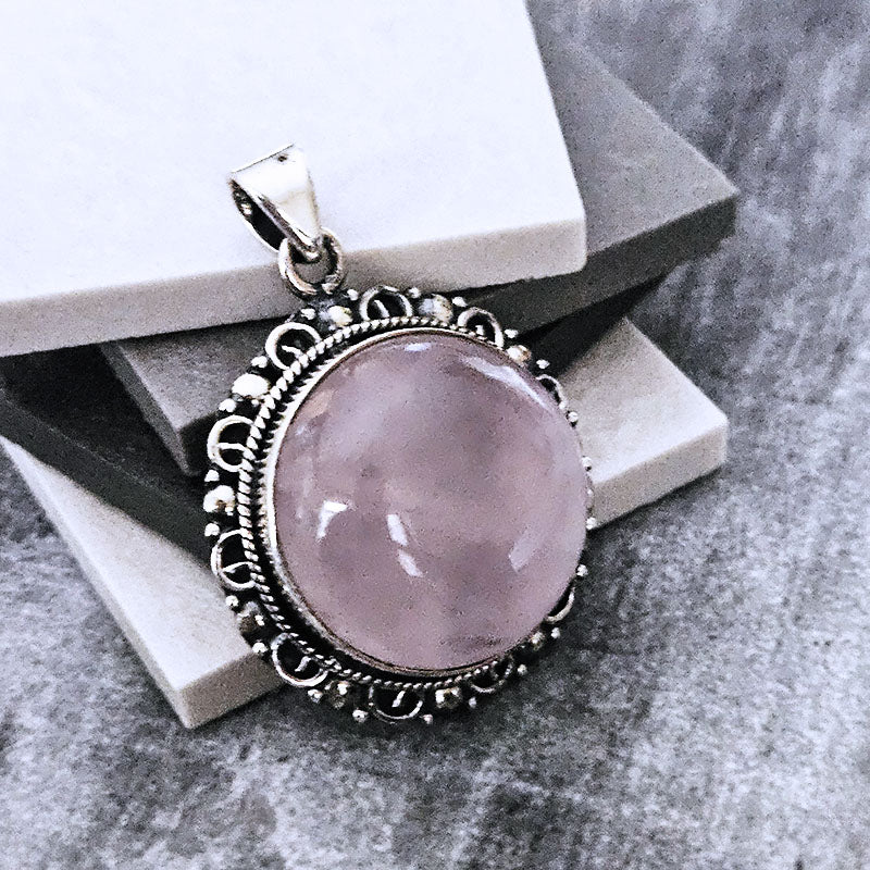 Pink stone pendant with silver frame on a textured surface