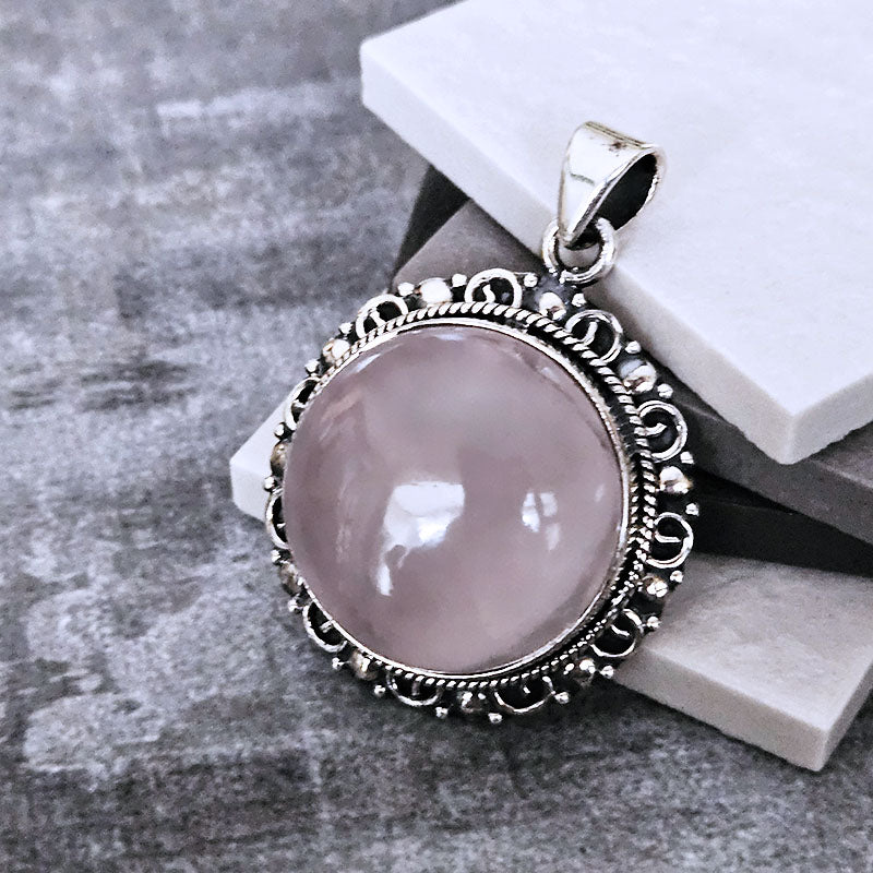 Pink stone pendant with silver decorative frame on a gray surface
