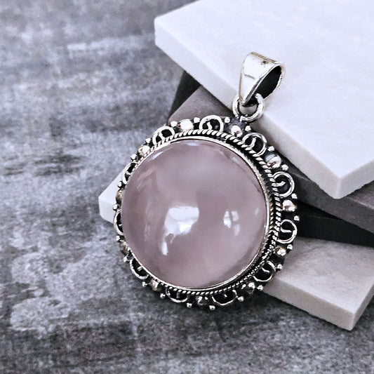 Pink stone pendant with silver decorative frame on a gray surface