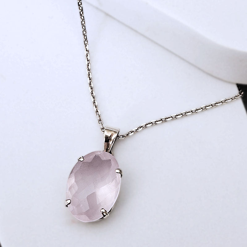 A silver chain necklace with an oval faceted light pink gemstone pendant, displayed on a clean white surface.