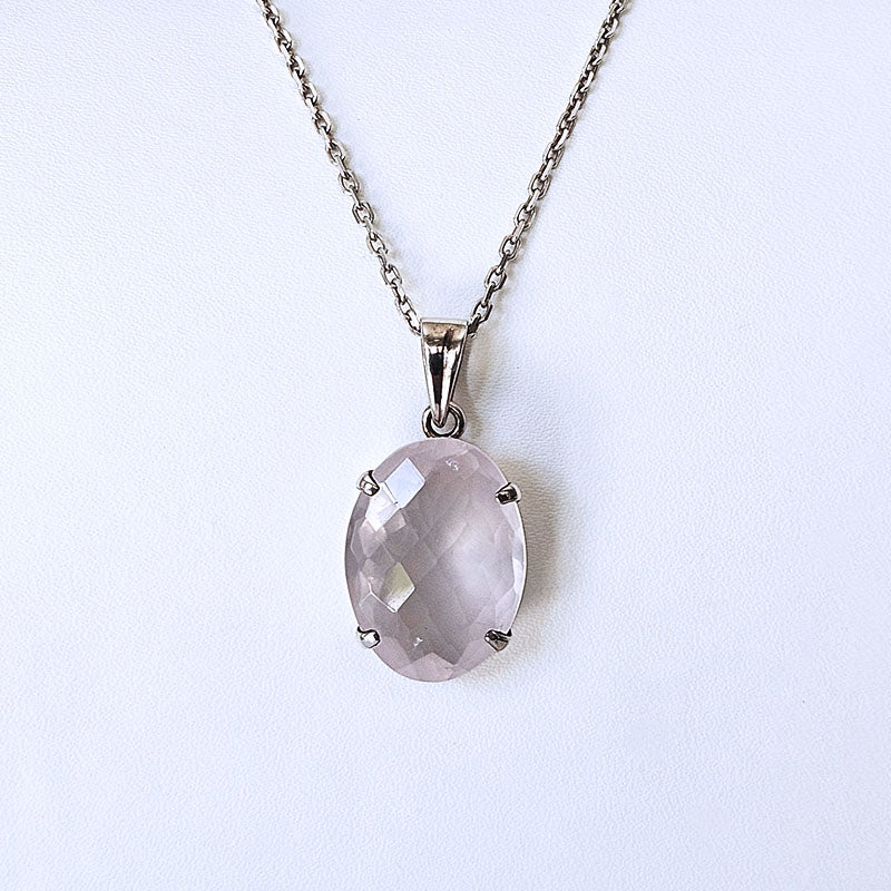 An oval-cut pale pink faceted gemstone pendant in a silver-toned setting, suspended from a matching silver-toned chain against a plain white background.