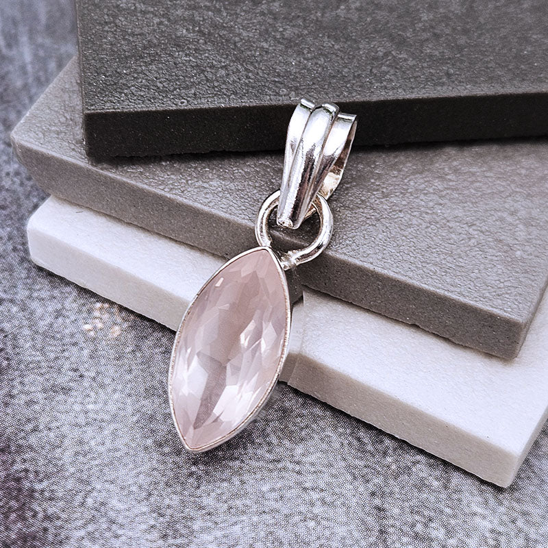 A silver pendant with a marquise-cut pale pink gemstone, displayed on stacked gray and white blocks.