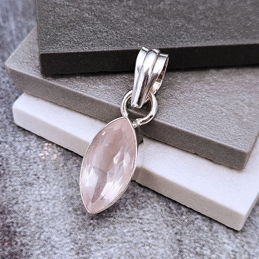 A silver pendant with a marquise-cut pale pink gemstone, displayed on stacked gray and white blocks.