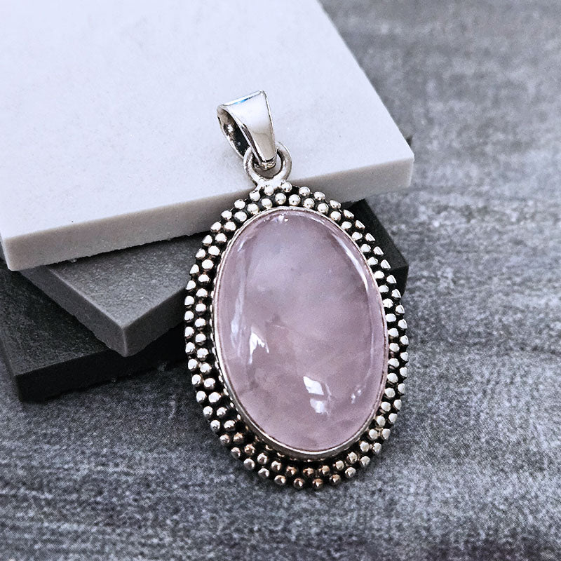Pink stone pendant with silver border on a gray surface