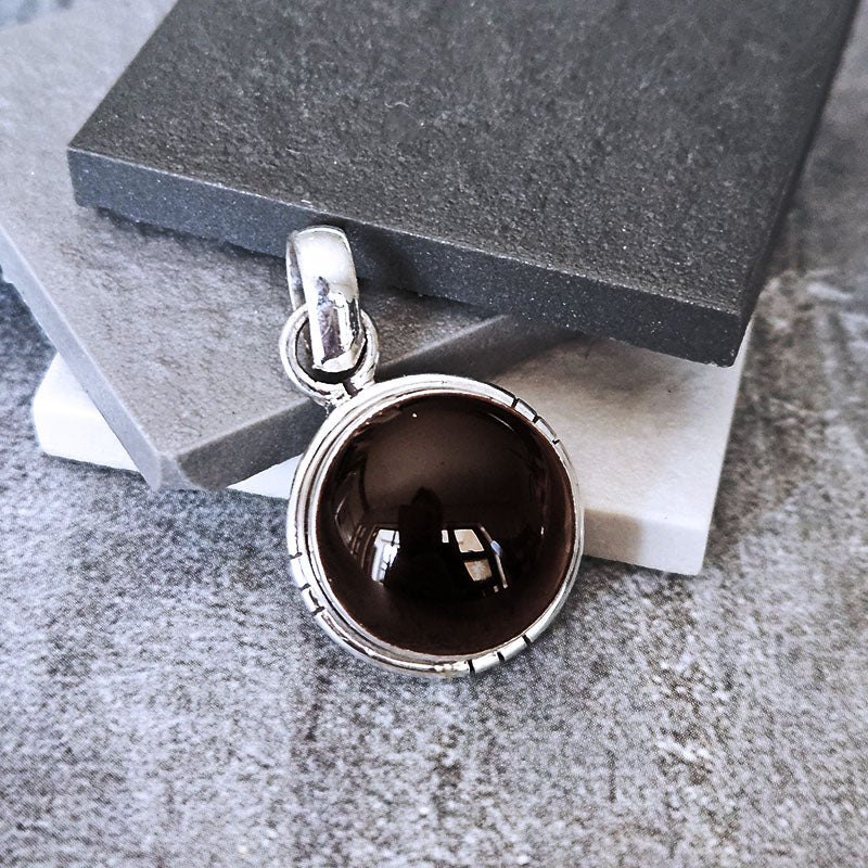 Silver pendant with a dark brown gemstone on a textured surface