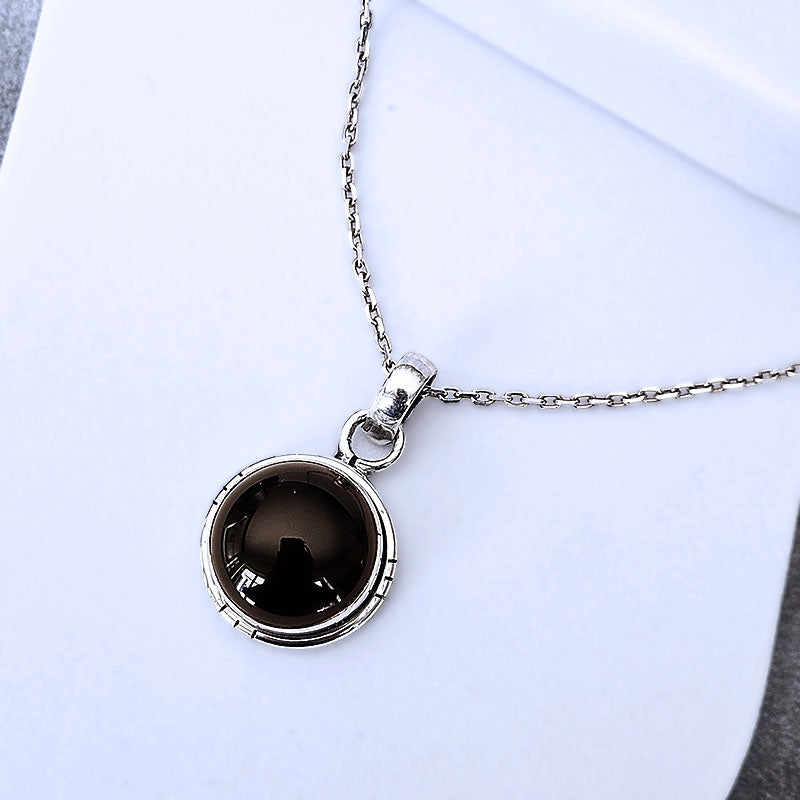Silver pendant with a dark gemstone on a light gray background
