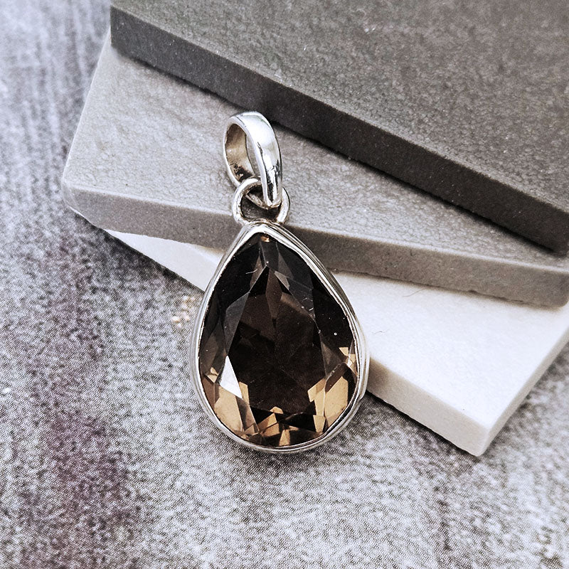Teardrop-shaped pendant with brown gemstone on a textured surface
