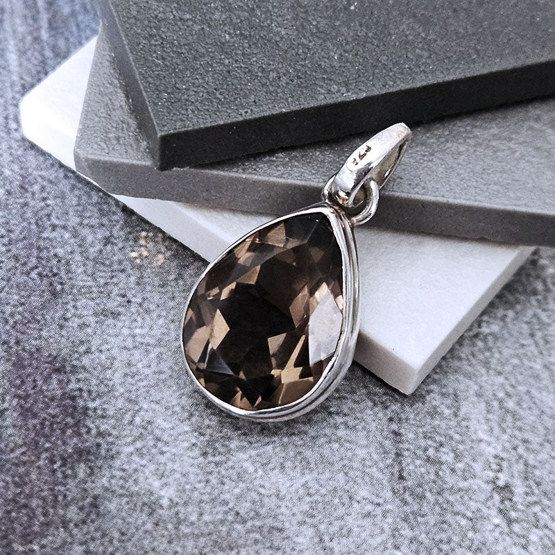 Teardrop-shaped smoky quartz pendant on a silver chain against a gray stone background
