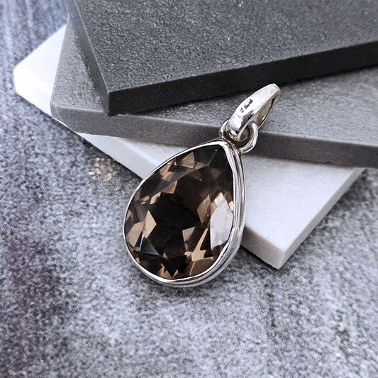 Teardrop-shaped smoky quartz pendant on a silver chain against a gray stone background