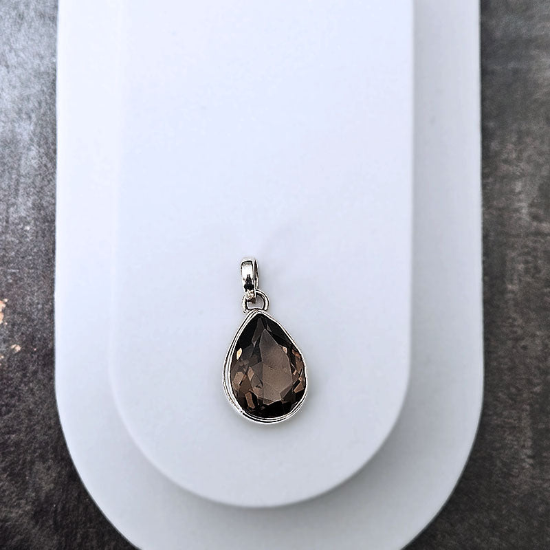 Teardrop-shaped smoky quartz pendant on a white stand with a gray background