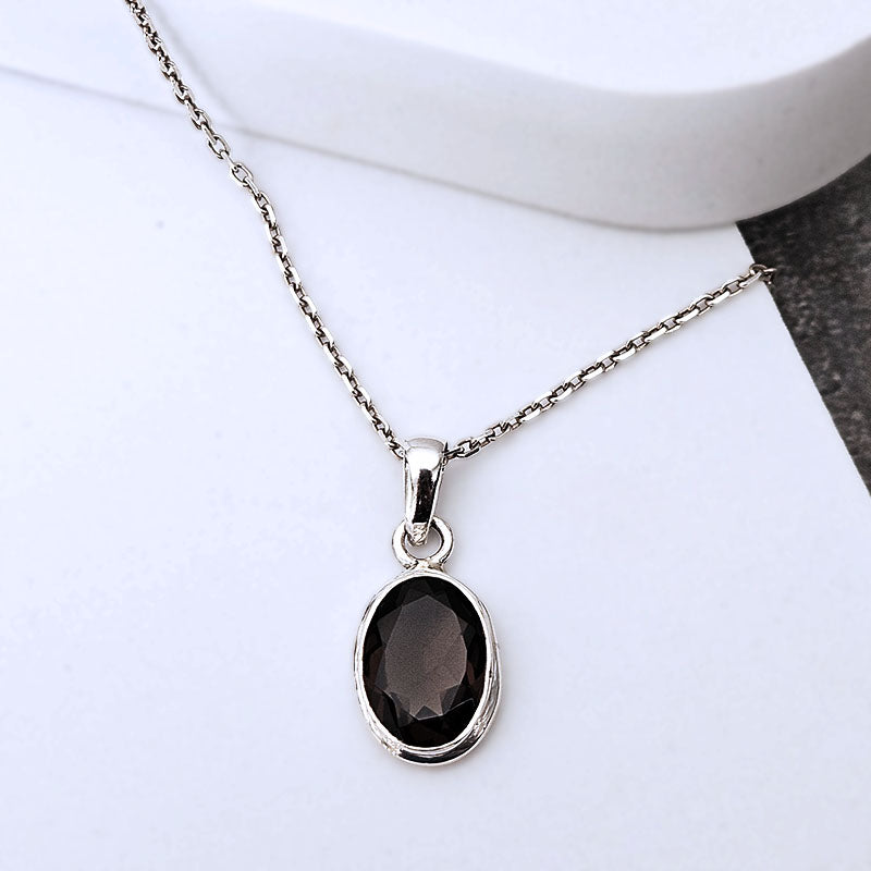 A silver chain necklace with an oval dark smoky gray gemstone pendant, displayed on a white surface.