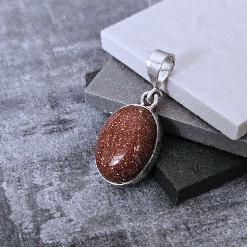 Brown Sunstone stone pendant with silver frame on a gray surface