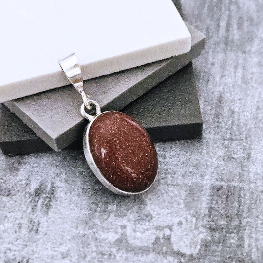 Brown Sunstone stone pendant on a silver chain against a textured surface