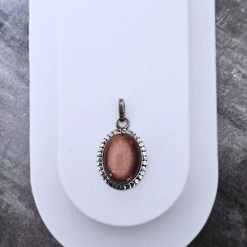 Sunstone oval pendant on a white stand with a gray textured background