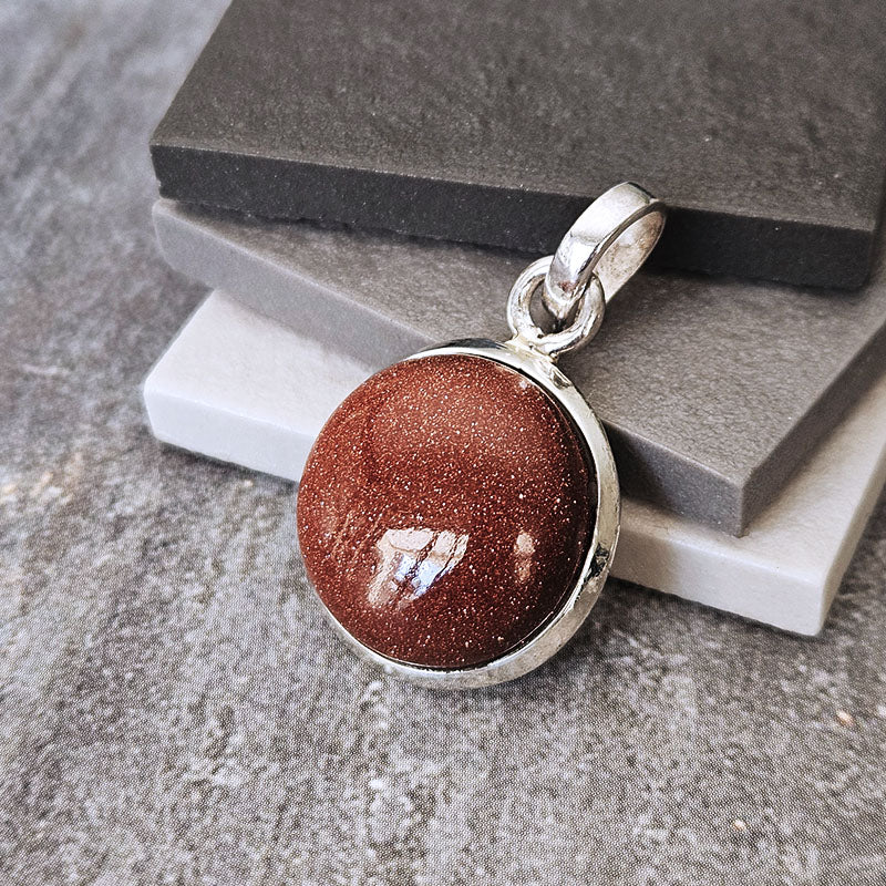 Brown stone pendant with silver setting on a textured surface