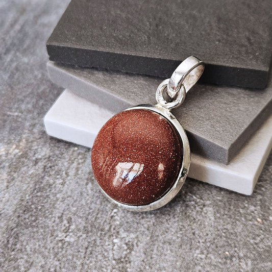 Brown stone pendant with silver setting on a textured surface