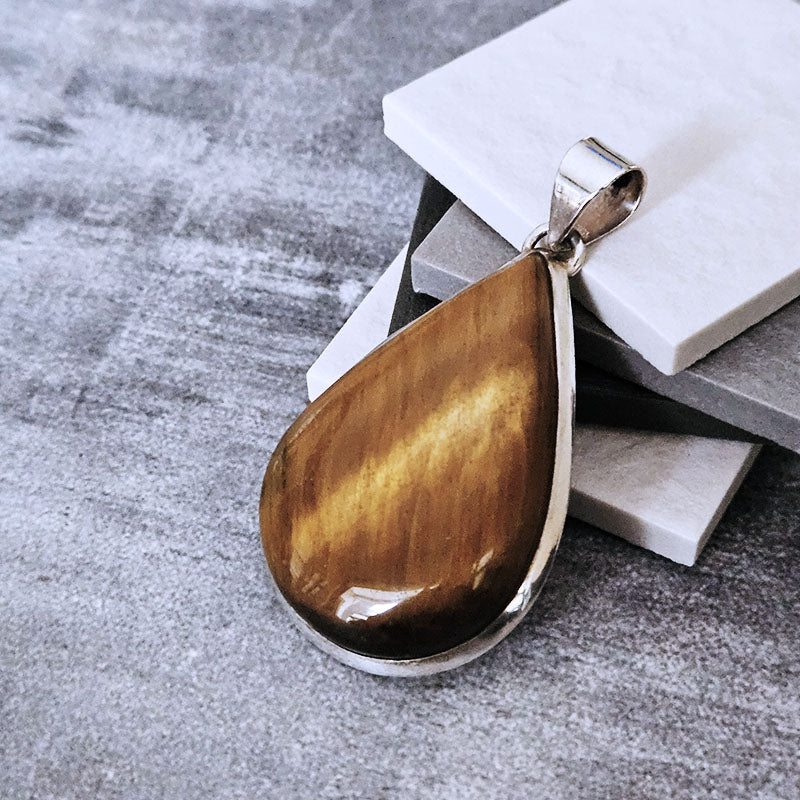 Teardrop-shaped pendant with brown stone on a gray surface
