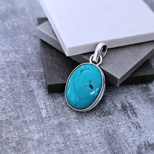 Turquoise pendant with silver setting on a textured surface