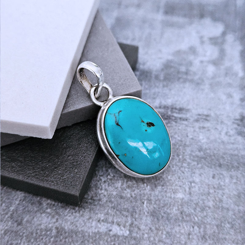 Turquoise pendant with silver frame on a textured surface