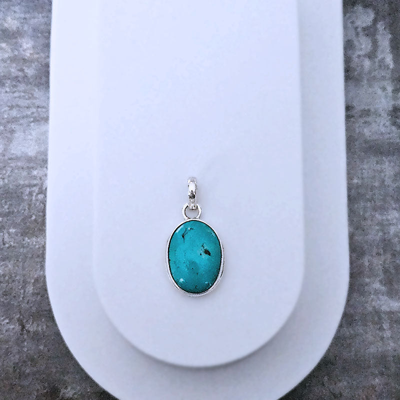 Turquoise pendant on a white stand with a textured gray background