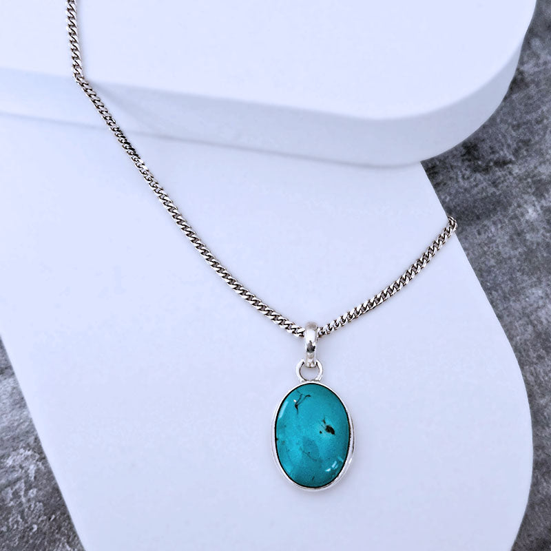 Turquoise pendant necklace on a white stand with a gray textured background