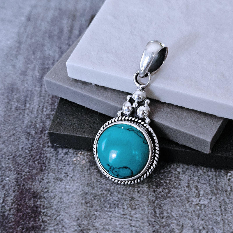 Turquoise pendant with silver chain on a stone surface