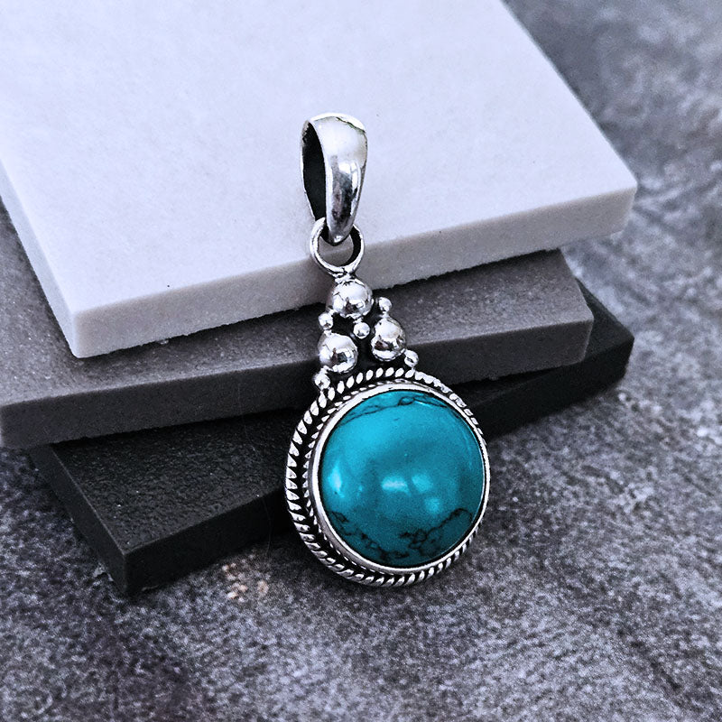 Turquoise pendant with silver frame on a textured surface