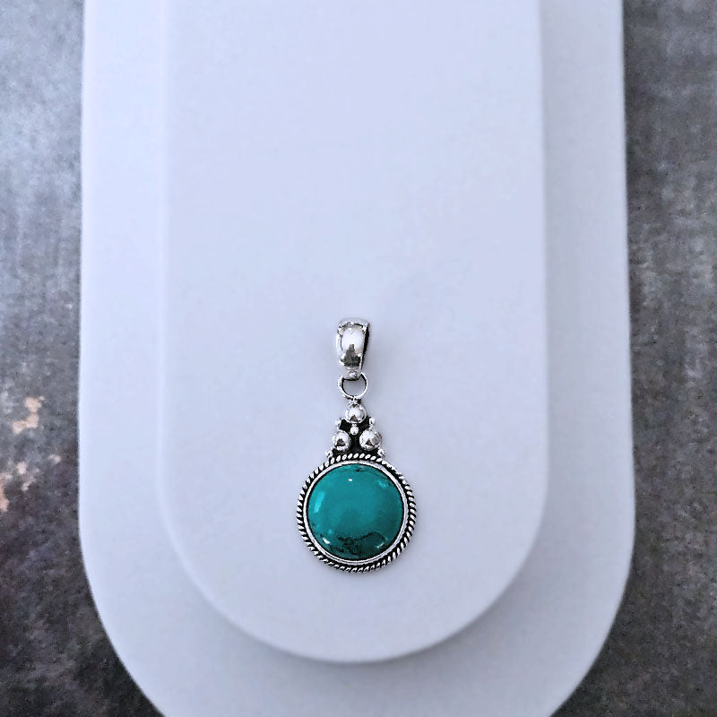 Turquoise pendant with silver setting on a white stand against a gray background