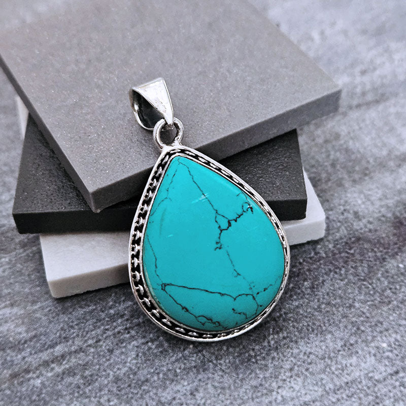 Teardrop-shaped Turquoise pendant set in sterling silver on a grey background
